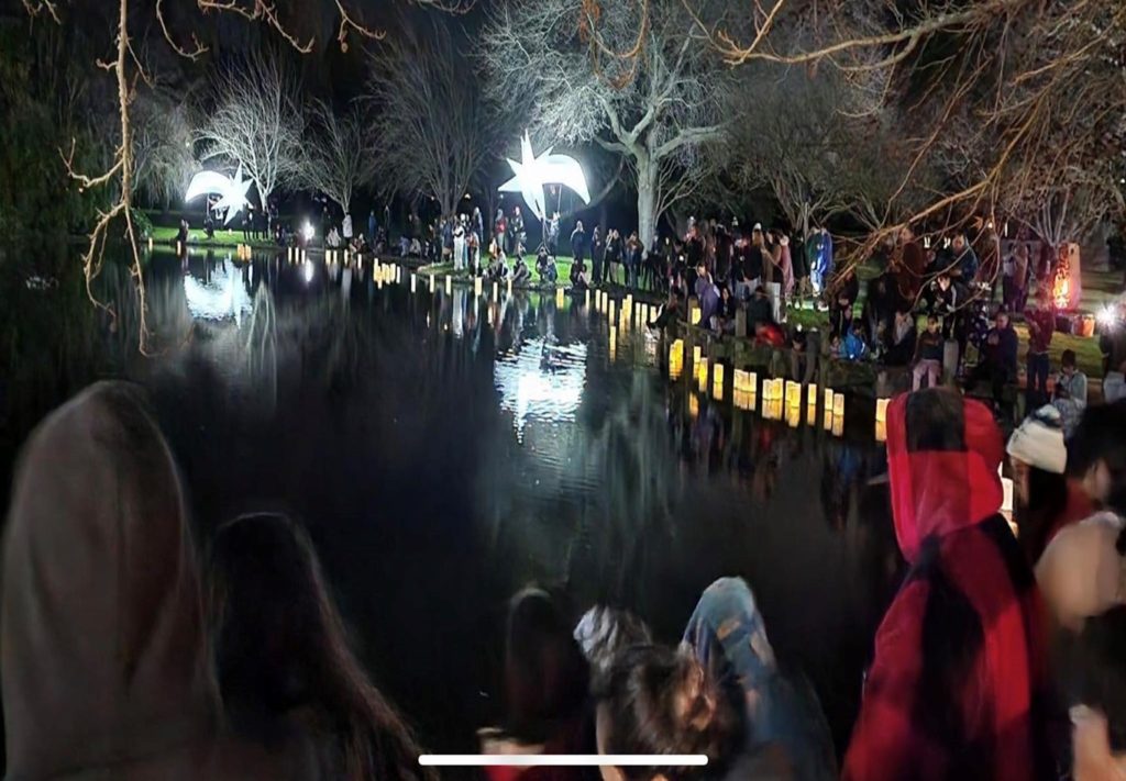 Cyclone affected whānau in Te Matau-a-Maui stand around water at night looking at the paper lanterns the made and floated in memory of their dead during Matariki 2023