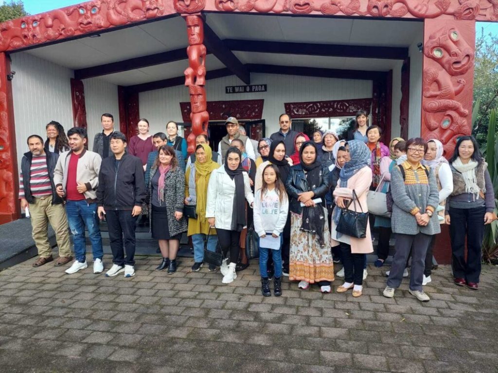 Whānau from four different ethnic communities pose for a photo outside the wharenui (meeting house) at Pakuranga Marae