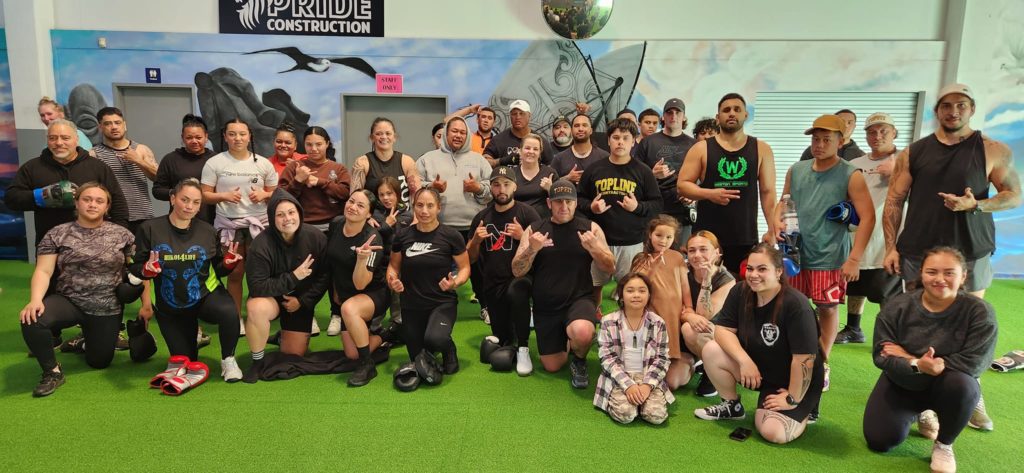 A group of about 40 people stand, kneel and sit for a photo in the Hikoi4Life gym. They're wearing sport wear and are soon to start working out.