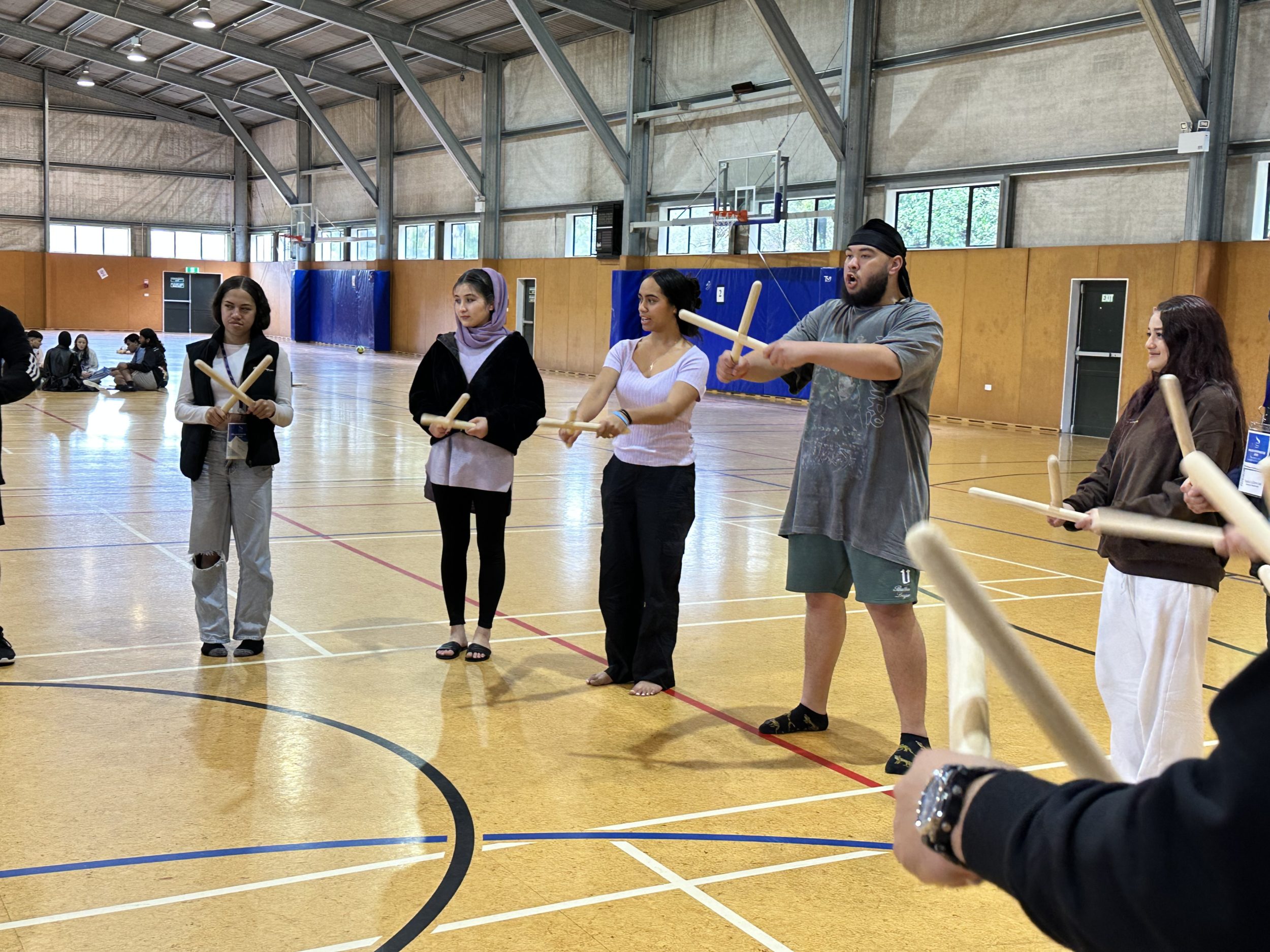 Rangatahi stand in a circle learning tī rākau during a Taha Tinana workshop