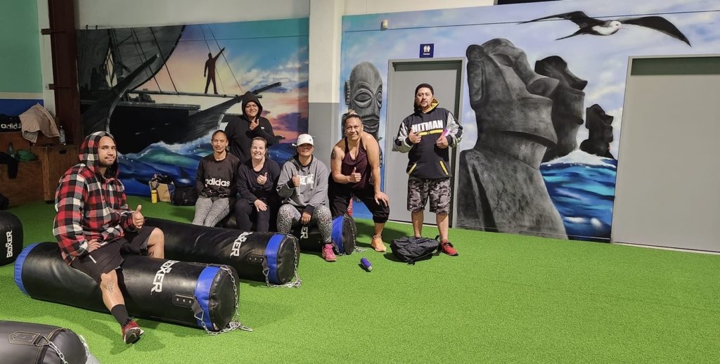 A small group of people sit on equipment and smile at the camera in the Hikoi4Life gym.