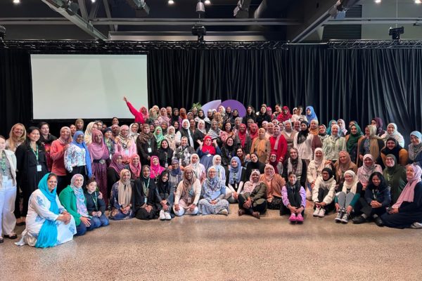 Muslim women from diverse communities who attended IWCNZ National Conference 2024 pose together for a groiu picture. Many are wearing colourful clothes and hijab, and are smiling at the camera.