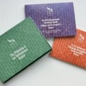 A picture of three coloured wallet folders containing the new E Tū Whānau measurement tools. They all have a woven texture on their covers. The green one is Te Pikitia a te Whānau Kete, the Purple one is Te Whakaoreore Aromatawai Hāpai ki te Hapori kete – The Community Mobilisation Assessment Toolkit,, and the orange wallet folder is E Tū Whānau Tikanga Rangahau – Community Kete