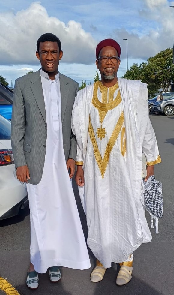 In this picture, two men who are part of Autism Noor stand beside each other, looking at the camera. They are dressed in jalabiyas. Mustafa, who looks like he is in his early 20s is on the left, with Modi, who is middle aged, on the right.