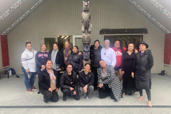 Te Ara Ki Hawaiki Roa wānanga participants are pictured outside a wharenui at Horouta Marae, Porirua . Fourteen people stand in two rows and are smiling at the camera.