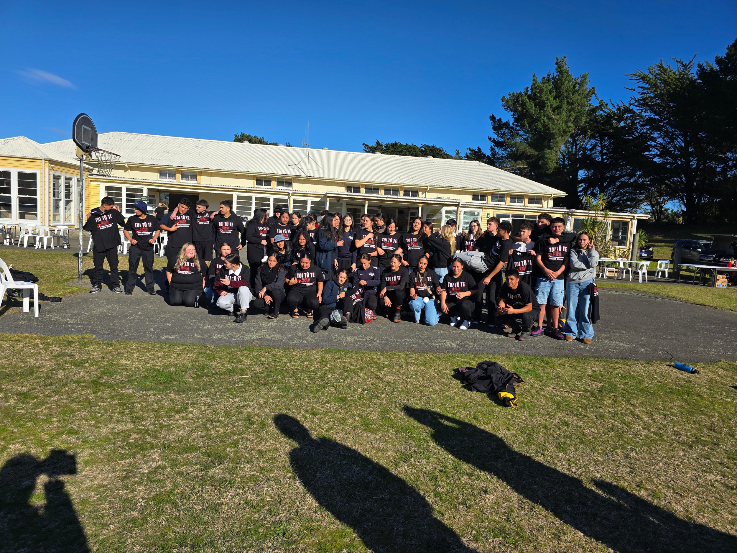 A big group of the rangatahi who attended Toi tū te Ora Rangatahi Symposium in Ōtaki pose for a photograph. People at the symposium used Te Whakaoreore to focus kōrero and action on their moemoeā for safe relationships. The group of about 50 people appear to be in their late teens. They all wear black Toi Tū Te Ora t-shirts.