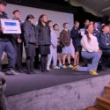 In this photo winners of the different categories in this year’s Ka Rere Te Manu Rangatahi Film Awards 2025 collect on stage. They fill the stage, with some kneeling and the others standing in a semi circle behind them. One teenage boy is holding a framed certificate. The young people range in age from pre-teens to teenagers.