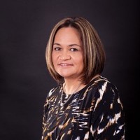 Marae Tukere, a member of Māori Reference Group, is pictured in this head and shoulders shot. Her hair is cut in a short bob, she wears smart, dark coloured clothing and is smiling at the camera. 