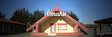 This image shows the whare nui of Ōmahu, one of the marae hosting the open days. The picture shows the wharenui in gentle sunlight. General marae grounds and buildings are visible next to the wharenui. 