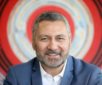 Piki Thomas, a member of Māori Reference Group, is pictured in this head and shoulders shot. he is dressed formally in a white shirt and blue jacket, looking directly at the camera with a gentle smile. 