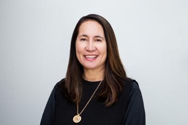 Maxine Shortland 2, a member of the Māori Reference Group, is pictured in a head and shoulders shot. She is dressed in smart balck clothes with a gold necklace. her long brown hair hangs down her shoulders and she is smiling at the camera. 