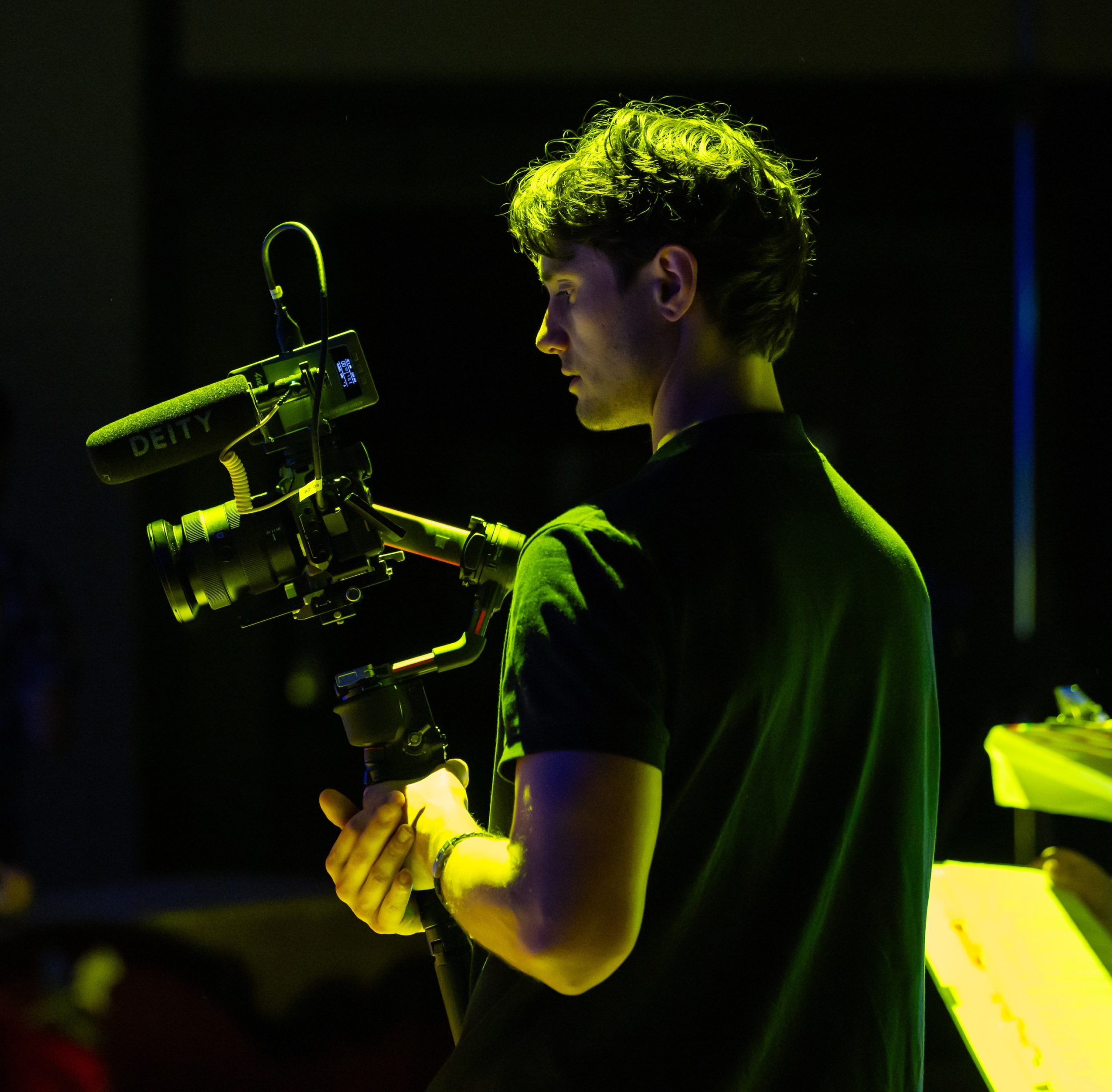 Isaac Te Reina is pictured while filmmaking from behind. the light is moody and he is holding a camera.