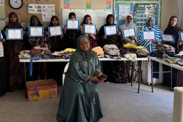 A group of women from migrant and former refugee communities are holding certificates for completion of a sewing course. One of the organisers, Fadumo Ahmed sits in the foreground.