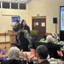 Candis Brunning stands in front of crowd of people while being recognised as a Rangatahi Kahukura – Emerging Leader at E Tū Whānau Kahukura Awards 2026. She is dressed in black and holds a certificate.