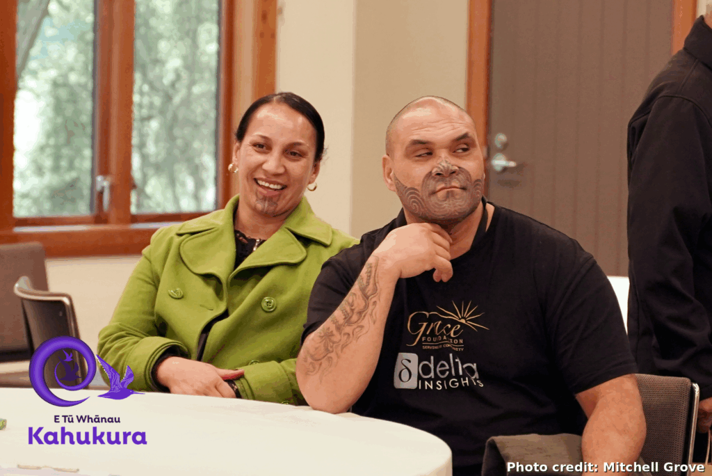 A man and woman are pictured sitting next to each other at Kahukura Workshop 2026. They are middle aged and both look relaxed and happy.