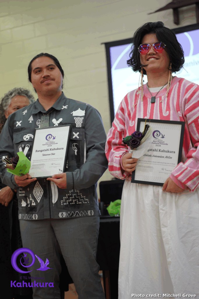 Two Young people, Tahuaroa Ohia and Waitahi Aniwaniwa McGee, stand with their Rangatahi Kahukura - Emerging Leaders certificates and flowers at the event.