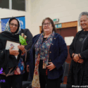 Fahima Saied is pictured wearing a headscarf and holding a Kahukura Awards certificate and flowers. She is with Heni Turner, E Tū Whānau Kaiwhakahaere, and Katie Murray. All three women are smiling.