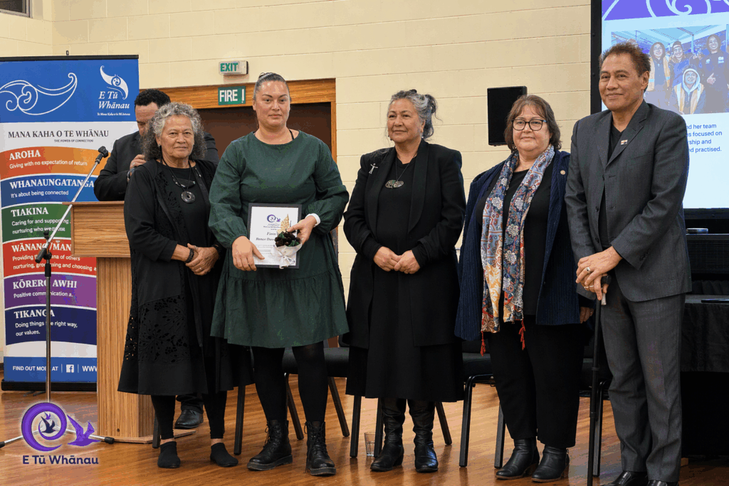 Renee Davis is pictured in a formal green dress at teh Kahukura Awards 2026 ceremony. She is holding a certificate and flowers and stands in a line with Katie Murray, Donna Matahaere-Atariki, E Tū Whānau Kaiwhakahaere Heni Turner, and Darrin Haimona.