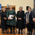 Renee Davis is pictured in a formal green dress at teh Kahukura Awards 2026 ceremony. She is holding a certificate and flowers and stands in a line with Katie Murray, Donna Matahaere-Atariki, E Tū Whānau Kaiwhakahaere Heni Turner, and Darrin Haimona.