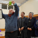 Esteban Espinoza, ALAC Founder and Director, celebrates ALAC being recognised as a finalist in the E Tū Whānau Ann Dysart Kahukura Award 2026. He has his hands raised in the air and is smiling. He is holding his finalist certificate and flowers. Behind him, people can be seen smiling and laughing.
