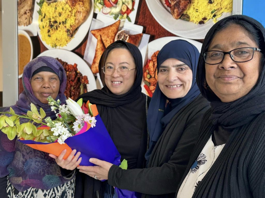 Fadumo Ahmed is pictured next to three women, all smiling and wearing headscarves. One of the women holds a bunch of colourful flowers.