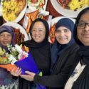 Fadumo Ahmed is pictured next to three women, all smiling and wearing headscarves. One of the women holds a bunch of colourful flowers.