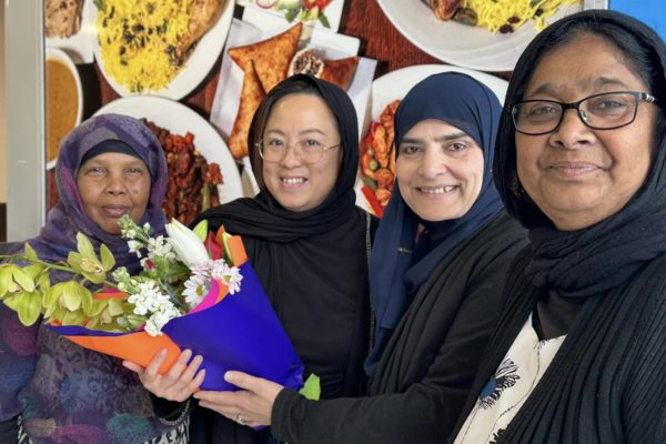 Fadumo Ahmed is pictured next to three women, all smiling and wearing headscarves. One of the women holds a bunch of colourful flowers.