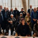A group representing Nannies Against P are pictured. There are about 30 people pictured, some of whom are in wheelchairs. Everyone is dressed formally.