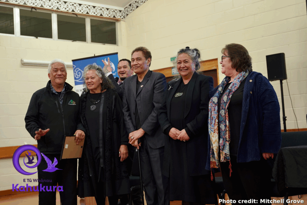 Rima Williams, Te Whānau Rangimarie kaimahi, stands with Katie Murray, Brent Mio, Darrin Haimona, Donna Matahaere-Atariki and Heni Turner, E Tū Whānau Kaiwhakahaere at the Awards.Riam looks very happy and is holding a framed certificate. Everyone is dressed formally.