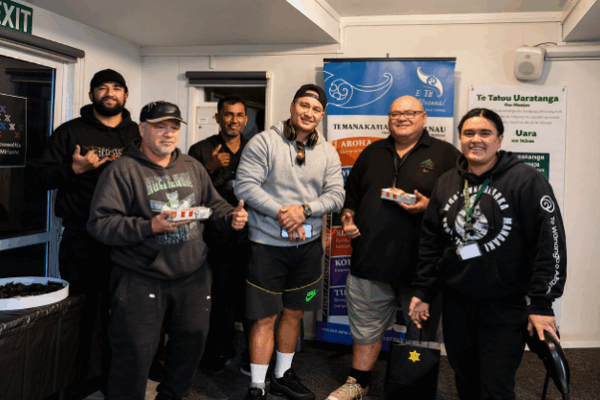 A group of Tsix e Whānau Rangimarie kaimahi are pictured together in front of a banner of the six E Tū Whānau values