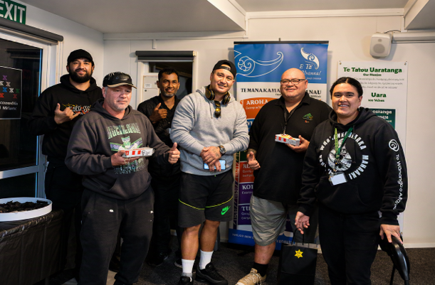 A group of Tsix e Whānau Rangimarie kaimahi are pictured together in front of a banner of the six E Tū Whānau values